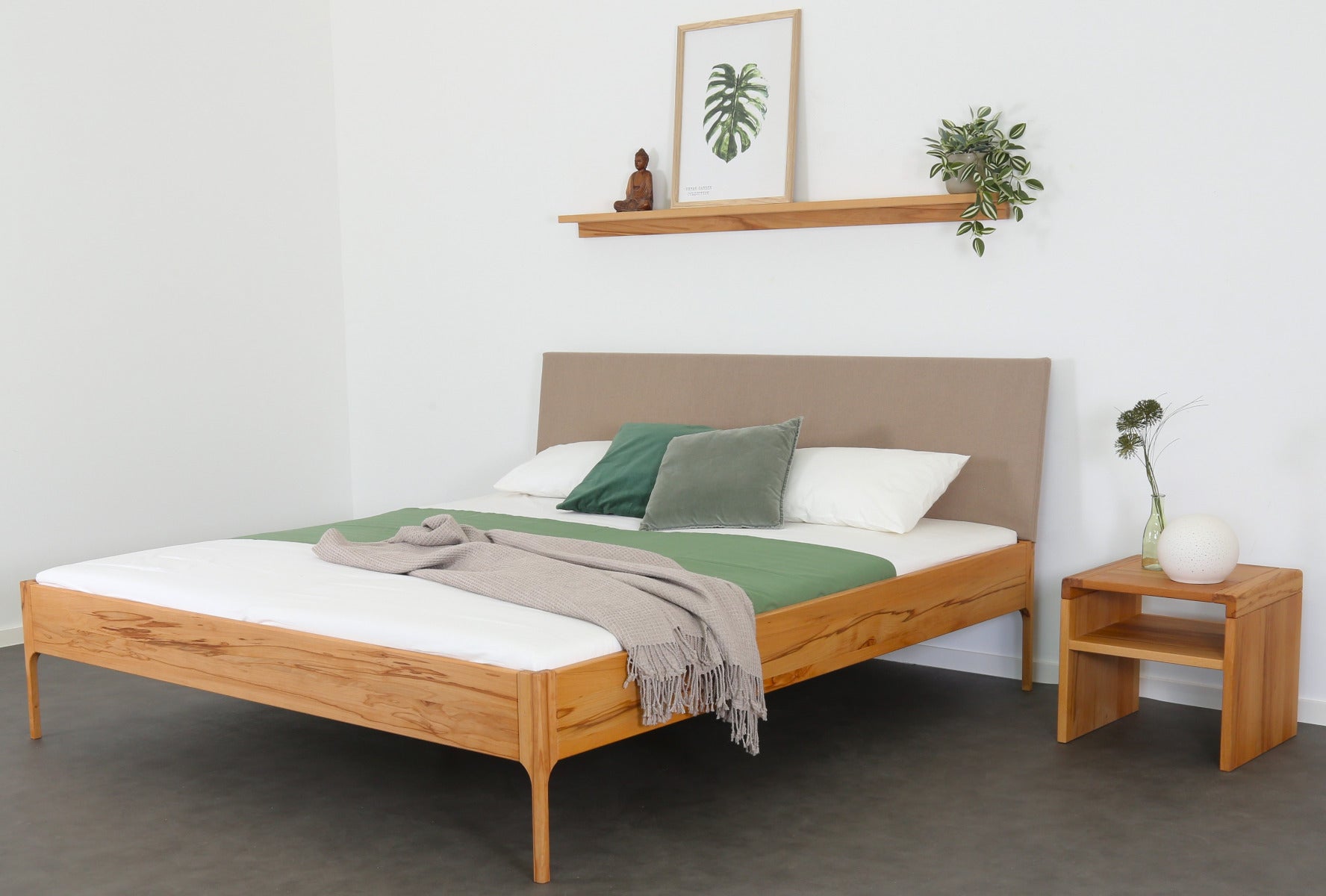 Schräge Frontalansicht von Bett Ona S in Kernbuche mit filigranen Füßen und rechteckiger Stofflehne in beige