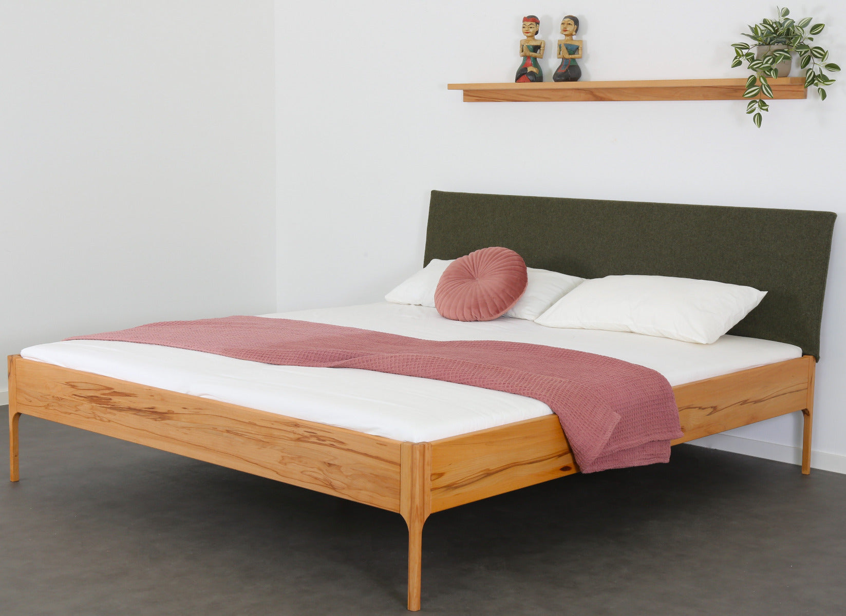 Schräge Frontalansicht von Bett Ona S in Kernbuche mit filigranen Füßen und rechteckiger Stofflehne in dunkelgrün