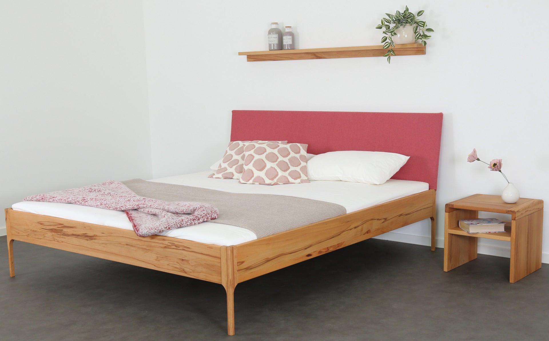 Schräge Frontalansicht von Bett Ona S in Kernbuche mit filigranen Füßen und rechteckiger Stofflehne in flamingo