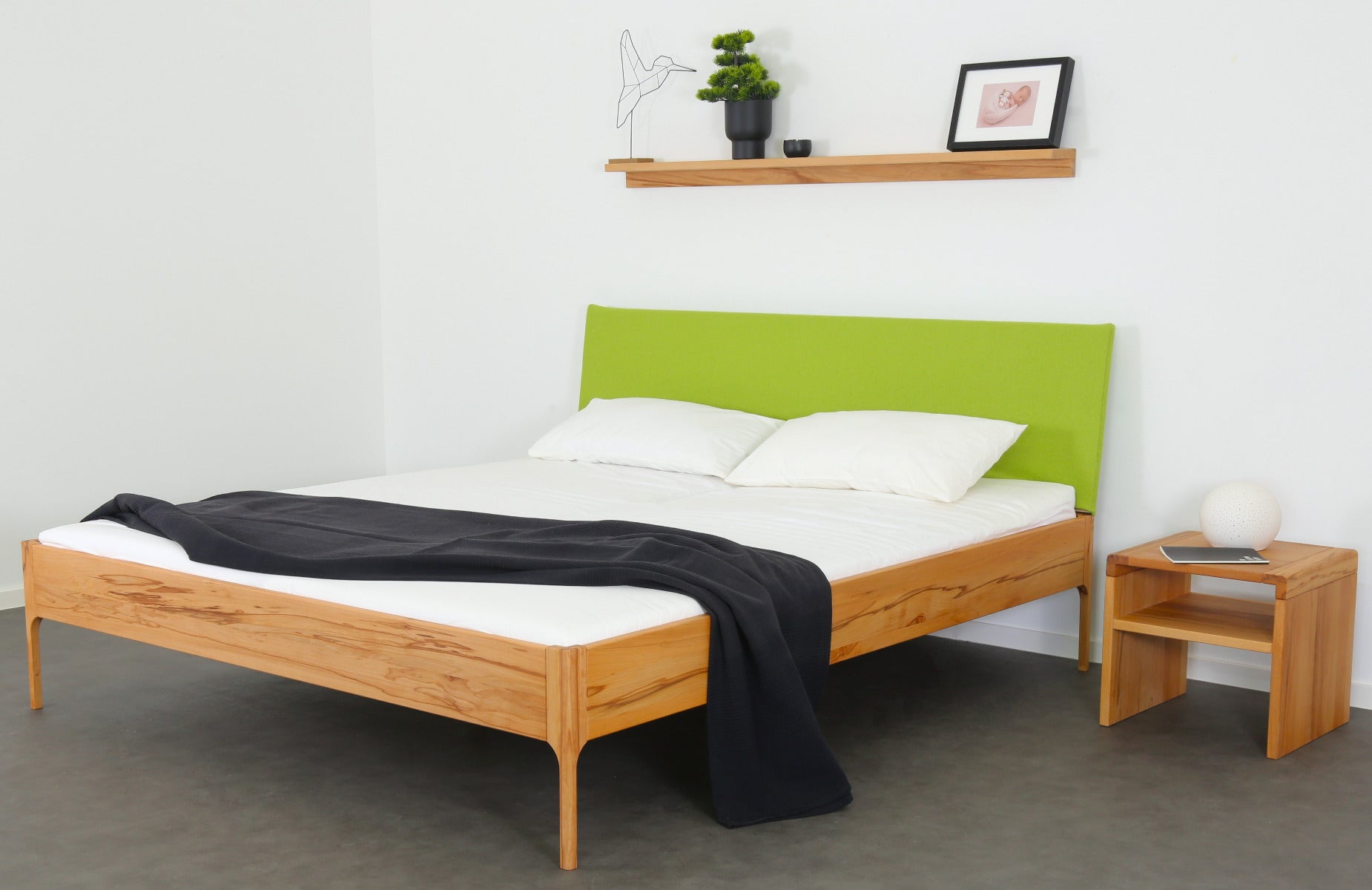 Schräge Frontalansicht von Bett Ona S in Kernbuche mit filigranen Füßen und rechteckiger Stofflehne in kiwi