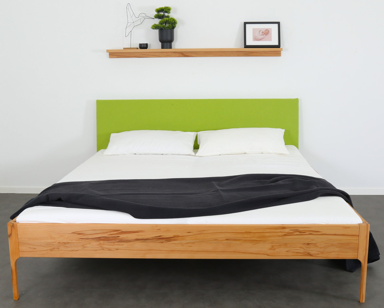 Frontalansicht von Bett Ona S in Kernbuche mit filigranen Füßen und rechteckiger Stofflehne in kiwi
