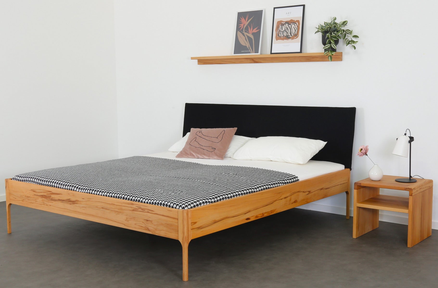 Schräge Frontalansicht von Bett Ona S in Kernbuche mit filigranen Füßen und rechteckiger Stofflehne in schwarz