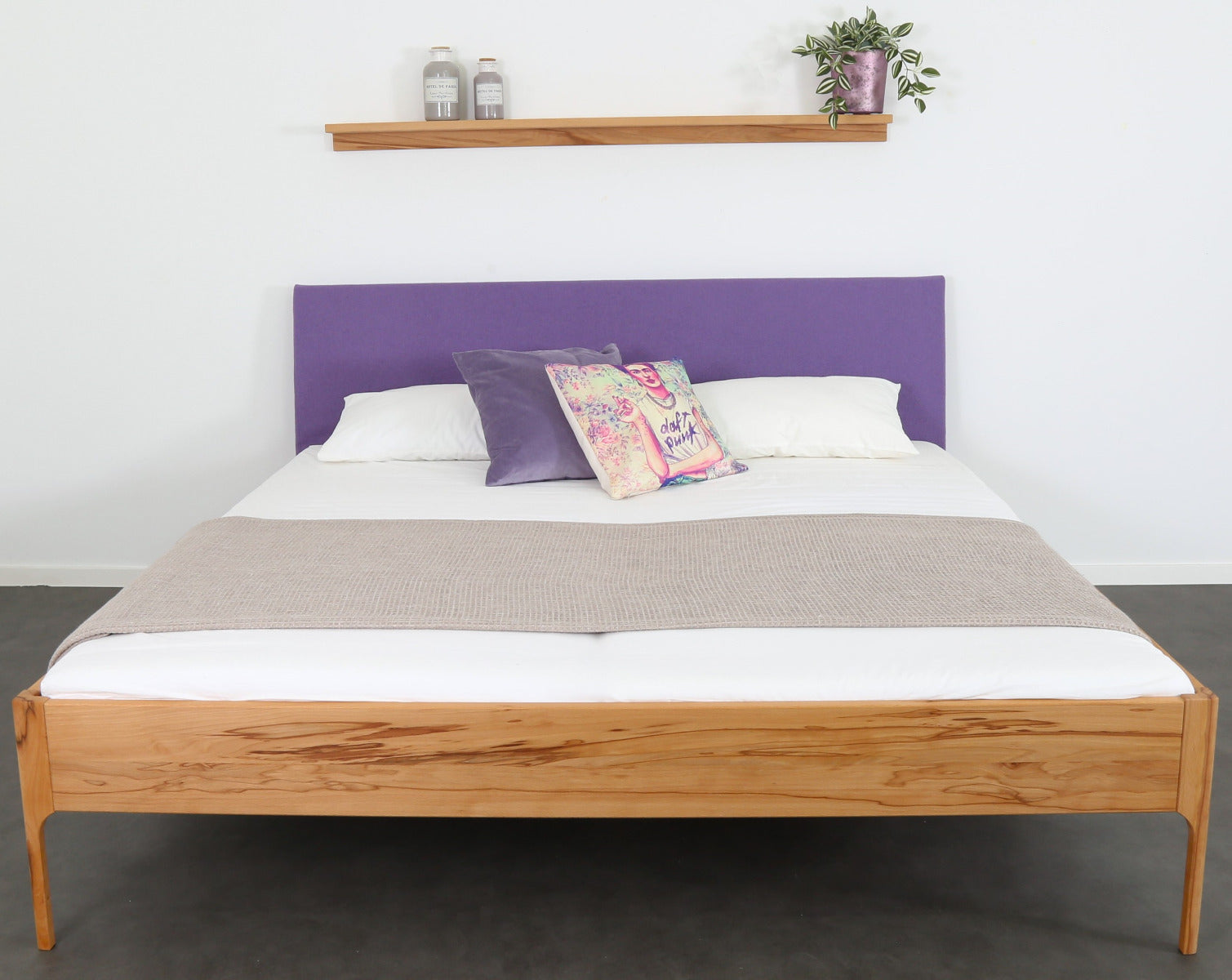 Frontalansicht von Bett Ona S in Kernbuche mit filigranen Füßen und rechteckiger Stofflehne in violett