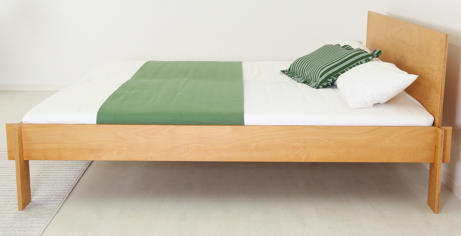 Seitenansicht des Bettes Mul in Buche-Multiplex mit der schlichten Lehne und dem simplen gesteckten Aufbau.