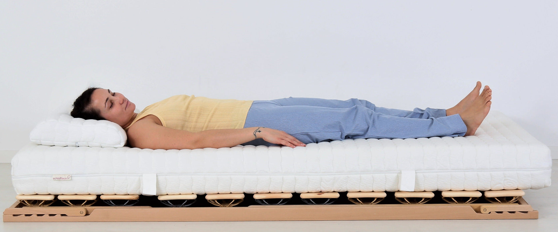 BIO-FORM-STRONG 7-Zonen Naturlatex-Matratze auf einem Tellerlattenrost. Darauf liegen eine Kissen und ein schlafender Mensch