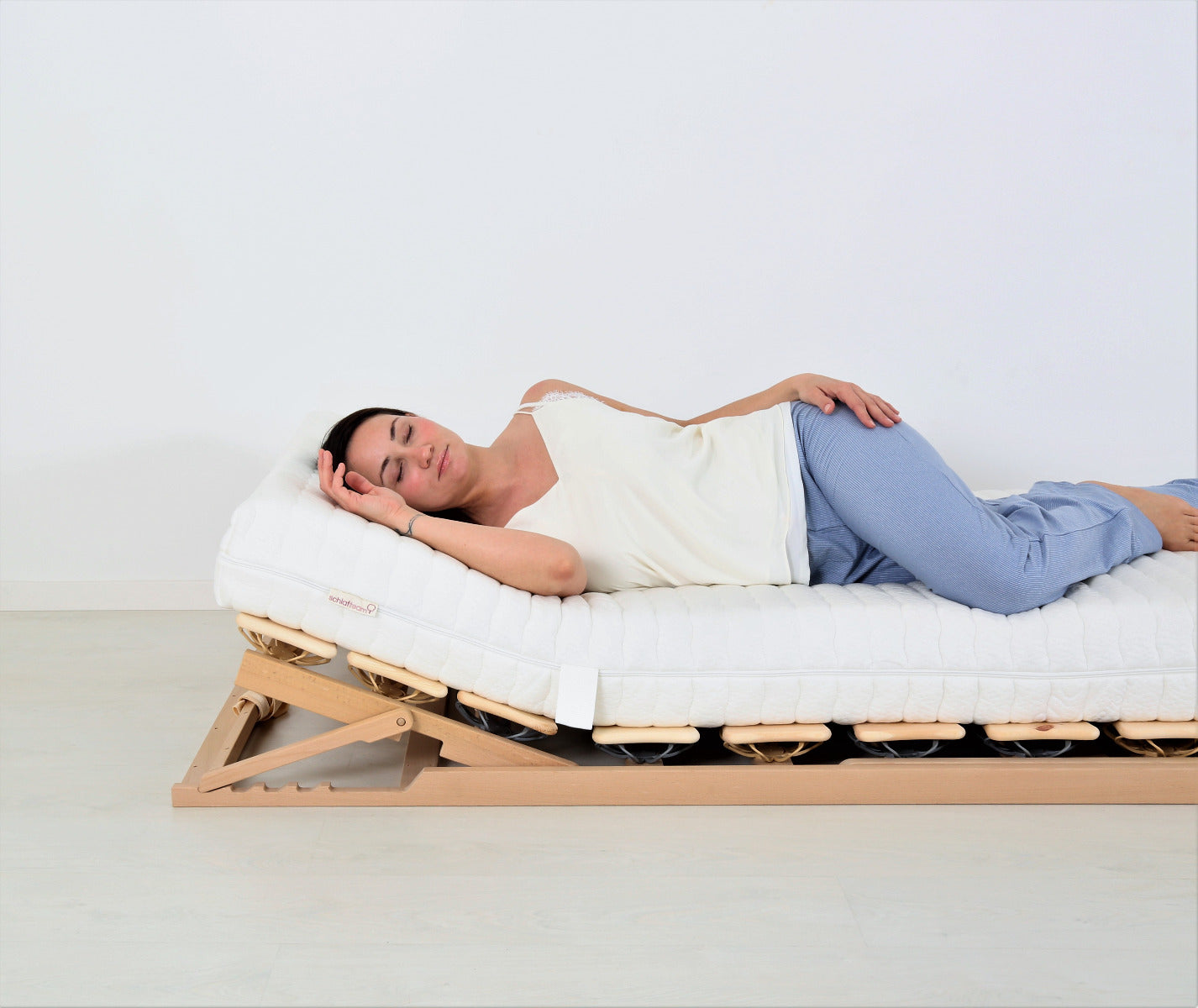 BIO-DOT-BUCHE Tellerlattenrost mit Matratze. Darauf ein Kissen und eine schlafende Person