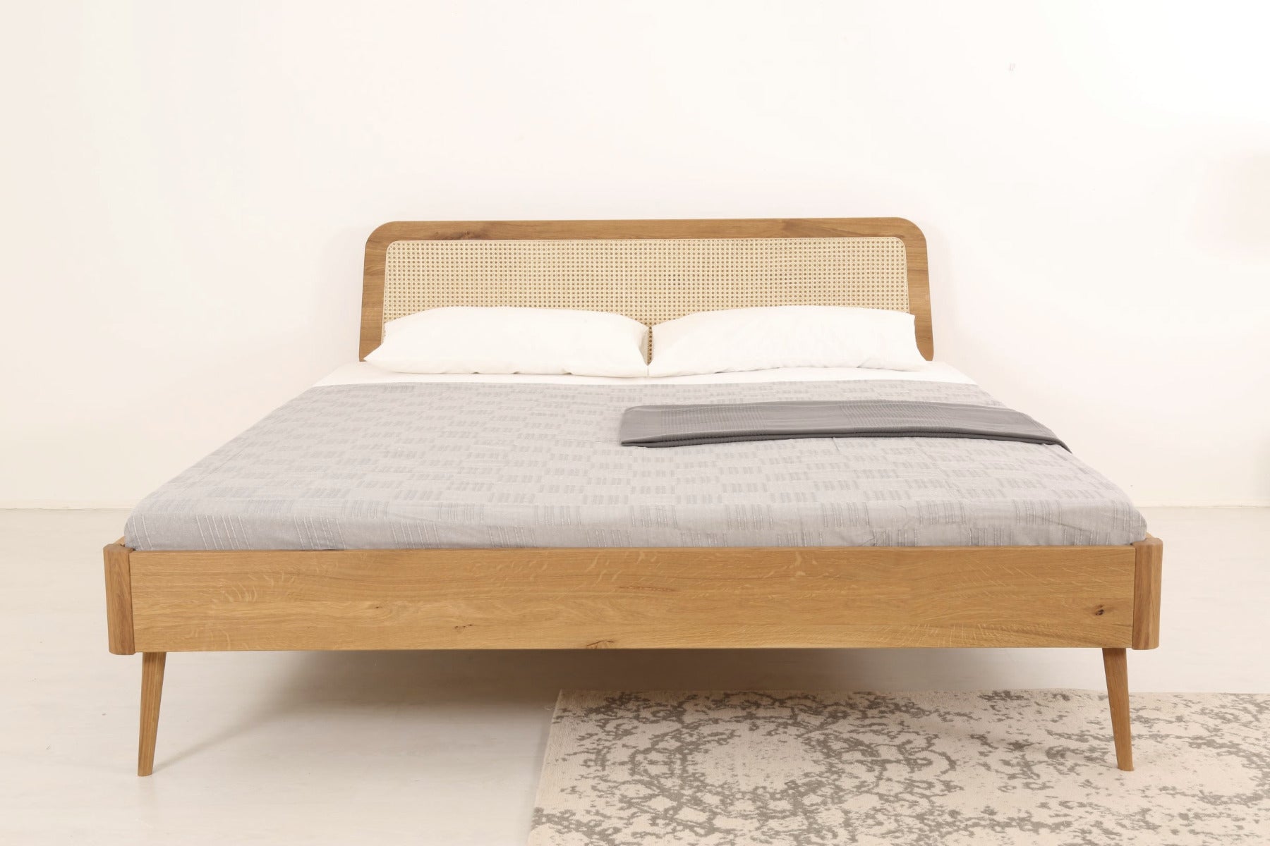 Frontalansicht von Bett Prina mit filigranen, kegelförmigen Füßen und Wiener-Geflecht-Lehne