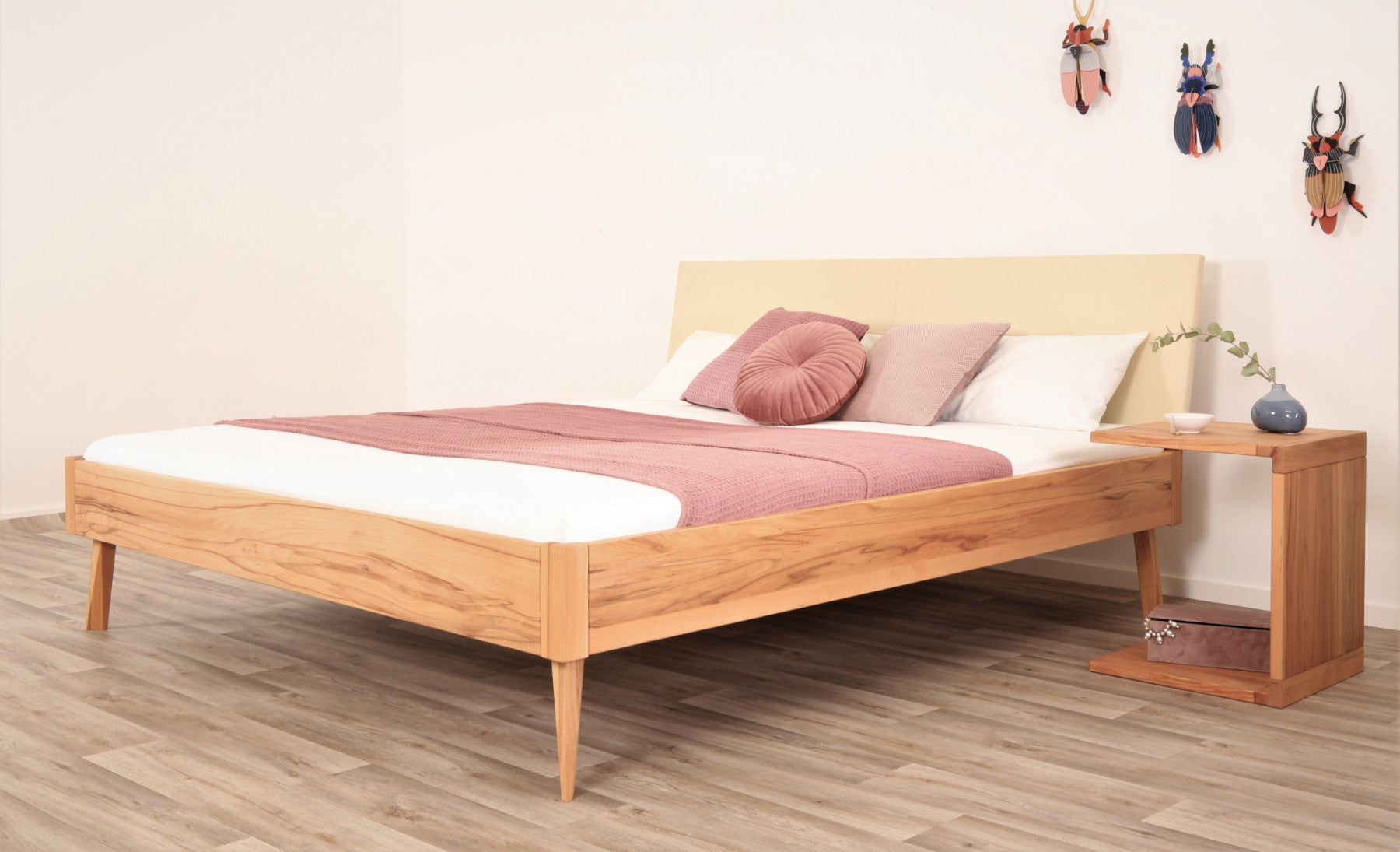 Schräge Frontalansicht von Bett Tuxa Premium mit filigranen Füßen und Rinderlederlehne in Elfenbein