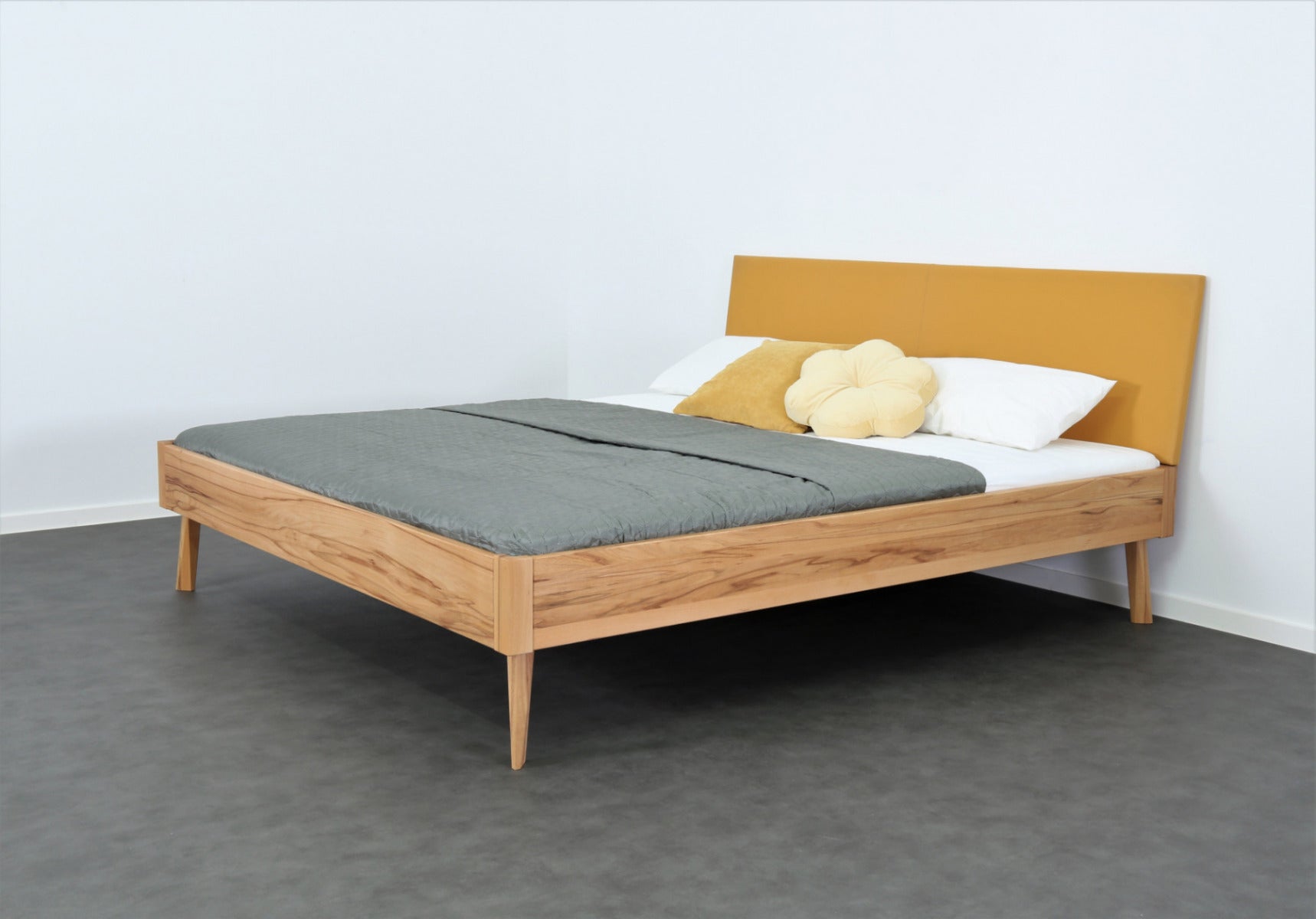 Schräge Frontalansicht von Bett Tuxa Premium mit filigranen Füßen und Rinderlederlehne in Kurkuma