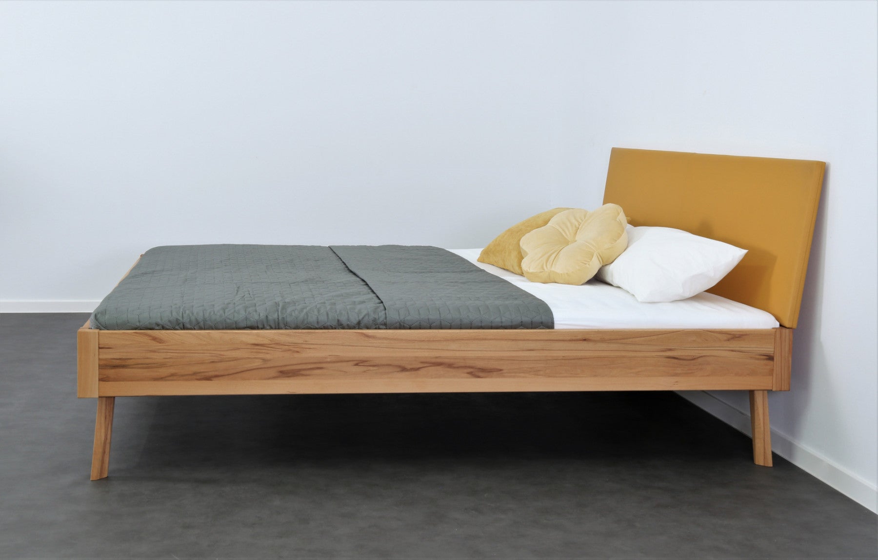 Seitenansicht von Bett Tuxa Premium mit filigranen Füßen und Rinderlederlehne in Kurkuma