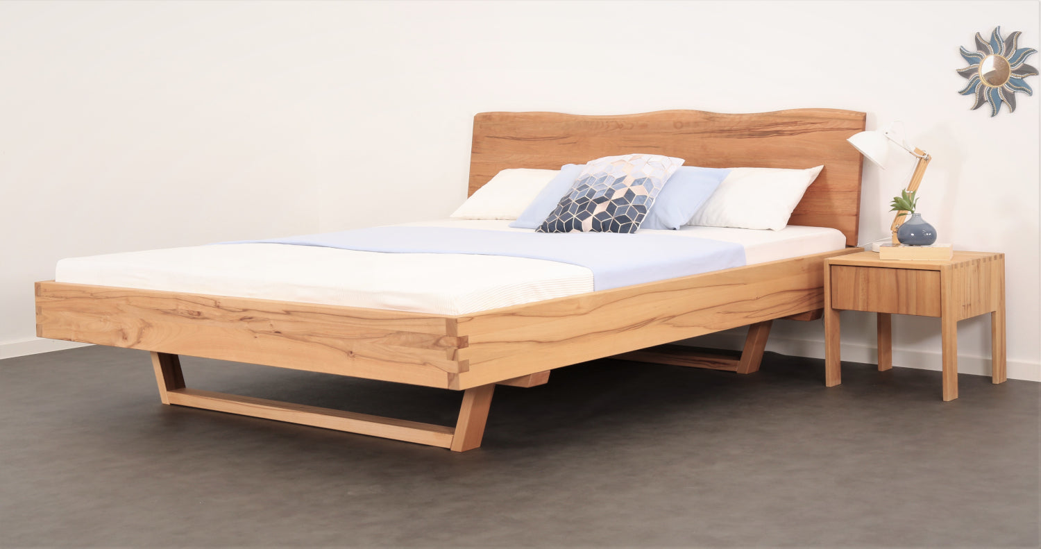 Schräge Frontalansicht von Bett Cofan mit Holzkufe und Baumkanten-Lehne.