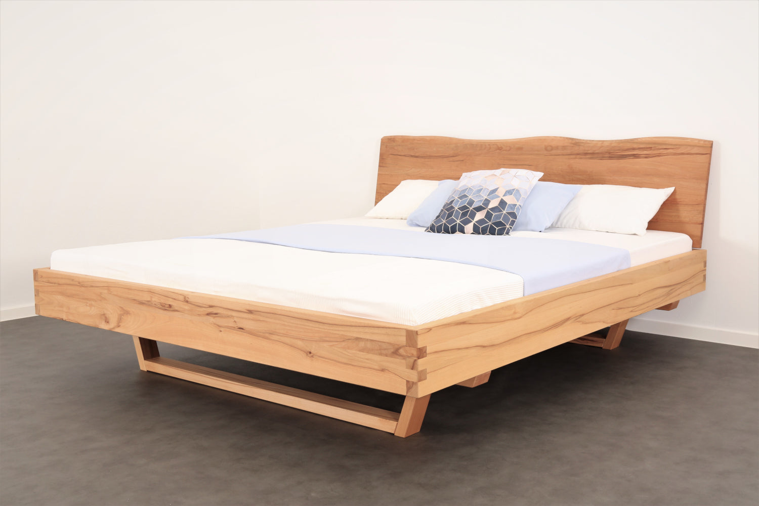 Schräge Frontalansicht von Bett Cofan mit Holzkufe und Baumkanten-Lehne.