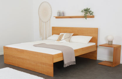 Schräge Frontalansicht von Bett Aikana in Buche mit Rückwand und Front mit gefrästem Streifen-Design 