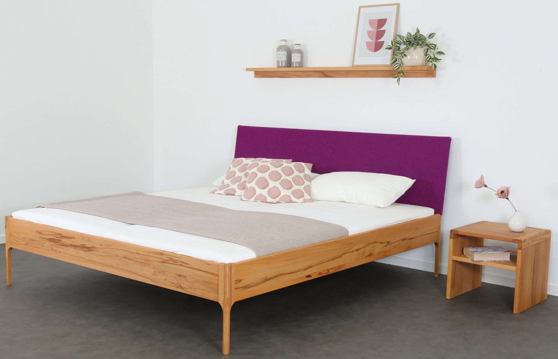 Schräge Frontalansicht von Bett Ona S in Kernbuche mit filigranen Füßen und  rechteckiger Stofflehne in beere