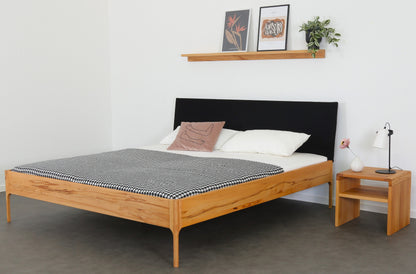 Schräge Frontalansicht von Bett Ona S in Kernbuche mit filigranen Füßen und  rechteckiger Stofflehne in schwarz