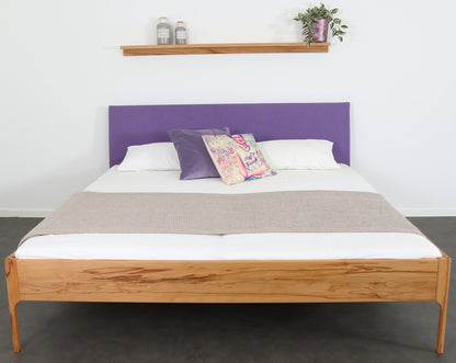 Frontalansicht von Bett Ona S in Kernbuche mit filigranen Füßen und  rechteckiger Stofflehne in violett