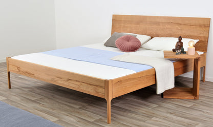 Schräge Frontalansicht von Bett Ona Zen in Kernbuche mit filigran gefräster Lehne und filigranen Füßen