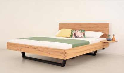 Schräge Frontalansicht von Bett Cofan in Kernbuche mit Kufe aus schwarz gebeizter/geölter Buche und schlichter, rechteckiger Lehne