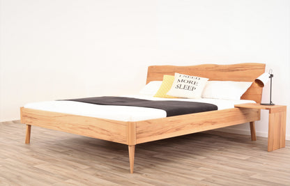Schräge Frontalansicht von Bett Tuxa Wood in Kernbuche mit filigranen Füßen und Baumkantenlehne
