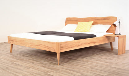 Schräge Frontalansicht von Bett Tuxa Wood in Kernbuche mit filigranen Füßen und Baumkantenlehne